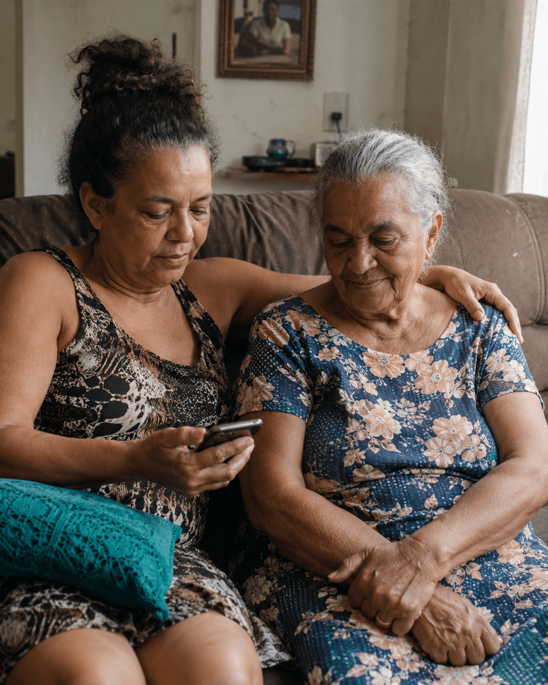 Uma filha de meia-idade e sua mãe idosa sentadas juntas, lado a lado, olhando para o celular em casa.